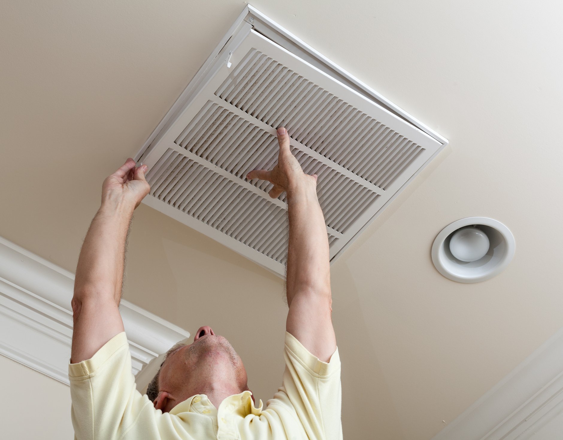 Senior Man Opening Air Conditioning Filter in Ceiling